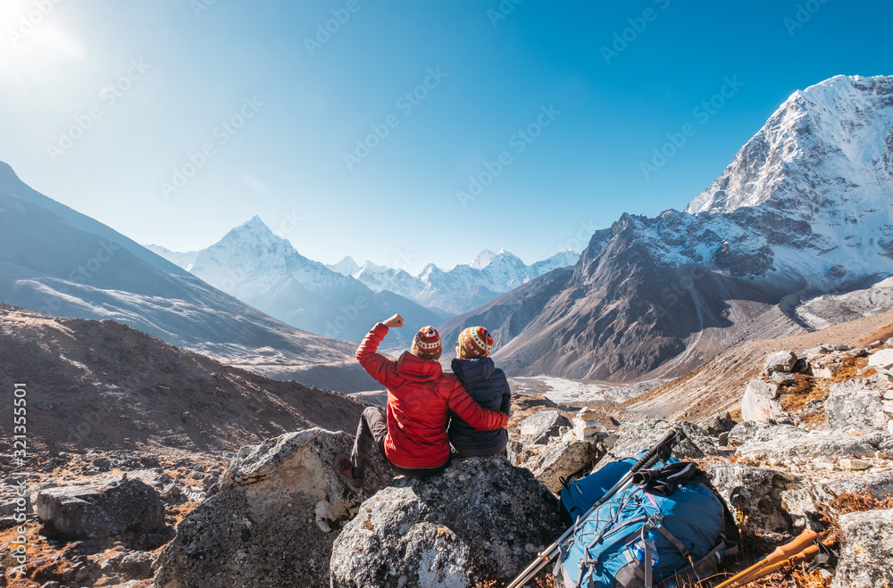 Young couple rejoicing on Everest Base Camp trekking route near Dughla 4620m. Backpackers left Backpacks and trekking poles and enjoying valley view with Ama Dablam 6812m peak and Tobuche 6495m - obrazy, fototapety, plakaty 
