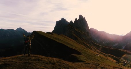 Wall Mural - aerial view. young man hiking at seceda mountain raising arms to the sky on the peak at sunrise. bac