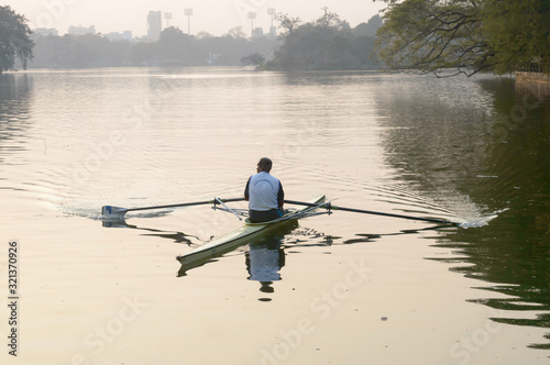 Photographie Individual Sports Speed Rower in Single scull crew rowing boat sliding racing shell on lake water oars in motion sitting sliding rigger seat doing exercise, fitness workout in sunset