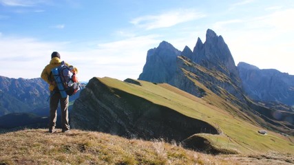 Wall Mural - young man hiking at seceda mountain leaving peak at sunrise. backpack, yellow jacket, boots, beanie.