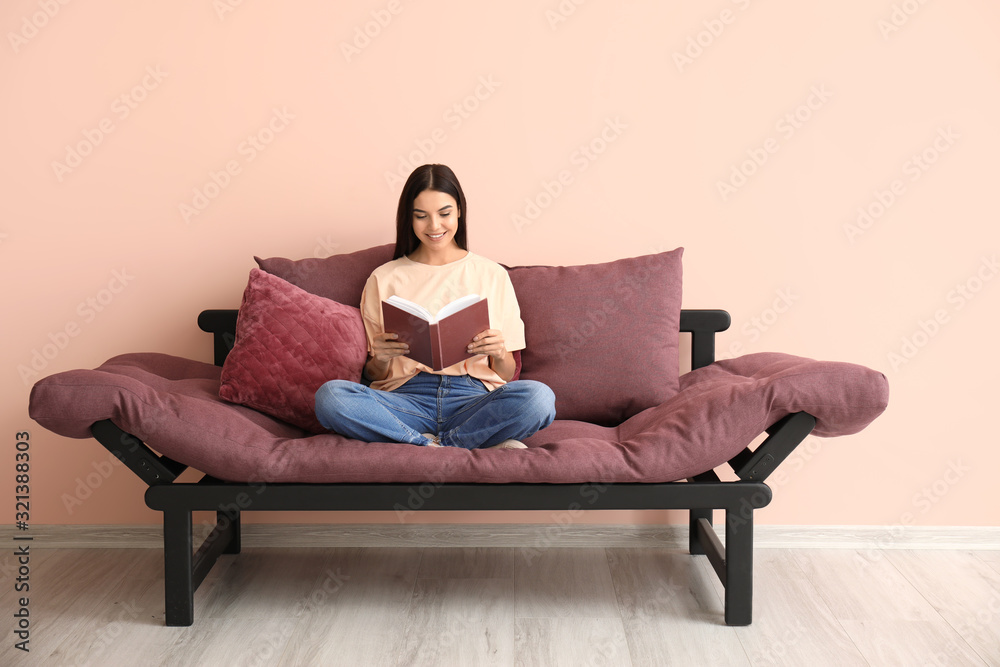 Young woman reading book while sitting on sofa at home