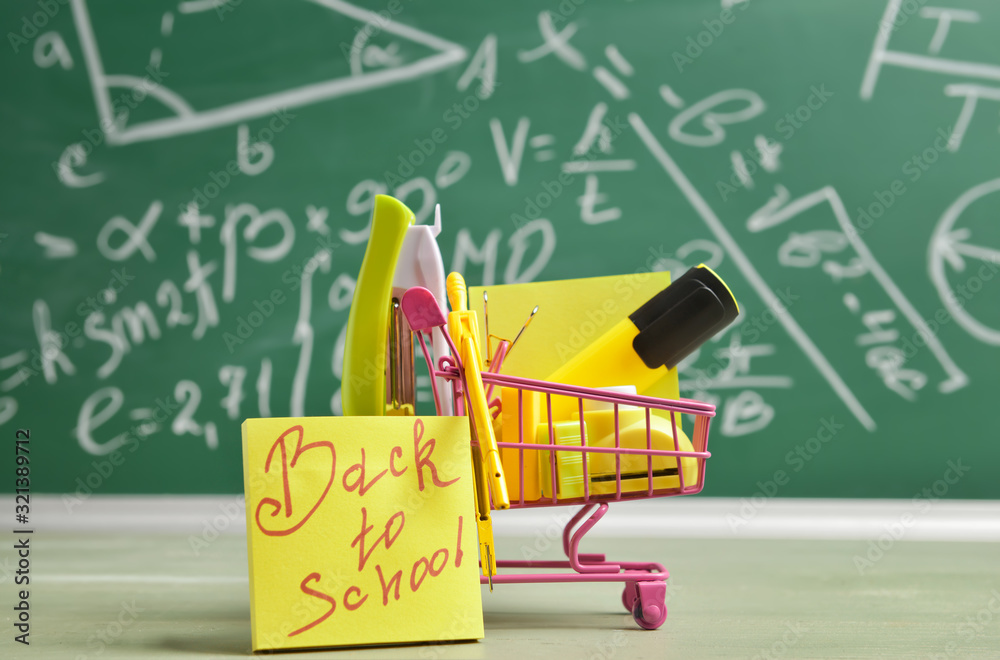 Shopping cart with school supplies on table in classroom