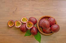 A Group Of Purple Skin Passion Fruit Plant, Sliced And Round Fruits In A Wooden Bowl On Wood Table, Top View Image And Copy Space