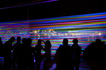 Silhouette Crowd of People Standing Outdoor in Front of Installation from Tensioned Neon Glowing Wires at Night. Concept of Modern Exhibitions and Technology Development