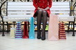 woman with shopping bags sits on a bench