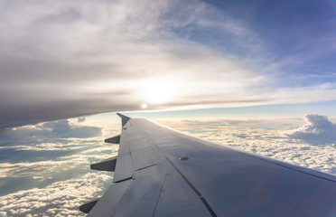 Sky scape view from clear glass window seat to the aircraft wing of the plane, traveling on the clouds and sunshine with blue sky