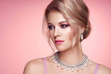 Wall Mural - Portrait Beautiful Blonde Woman with Jewelry. Elegant Hairstyle.  Beauty and Fashion Accessories. Perfect Make-Up. Pink Background