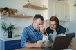 © Space_Cat - Young stressed Caucasian couple facing financials troubles, sitting at kitchen table with bills, checks and laptop computer and reading document from bank, looking frustrated and unhappy