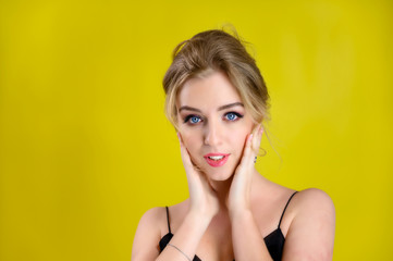 Glamorous beauty front view portrait of a pretty blonde model with excellent make-up and beautiful hairstyle on a yellow background in the studio. The concept of cosmetics, fashion and style.