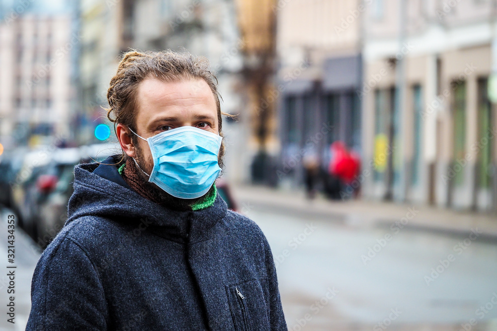 Handsome young European man in winter clothes on the street with a medical face mask on. Closeup of a 35-year-old male in a respirator to protect against infection with influenza virus or coronavirus - obrazy, fototapety, plakaty 