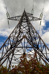 high voltage transmission tower blue sky and clouds background. The tower of high voltage transmition lines stands in the field so its legs are covered with bushes at the ground