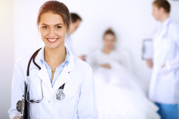 Wall Mural - Female doctor smiling on the background with patient in the bed and two doctors