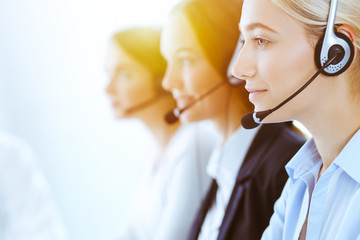 Group of diverse phone operators at work in sunny office. Handsome business woman with headphones consulting clients. Call center and business people concept