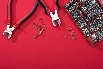 Wall Mural - Top view of tool box with pliers and nails on red surface