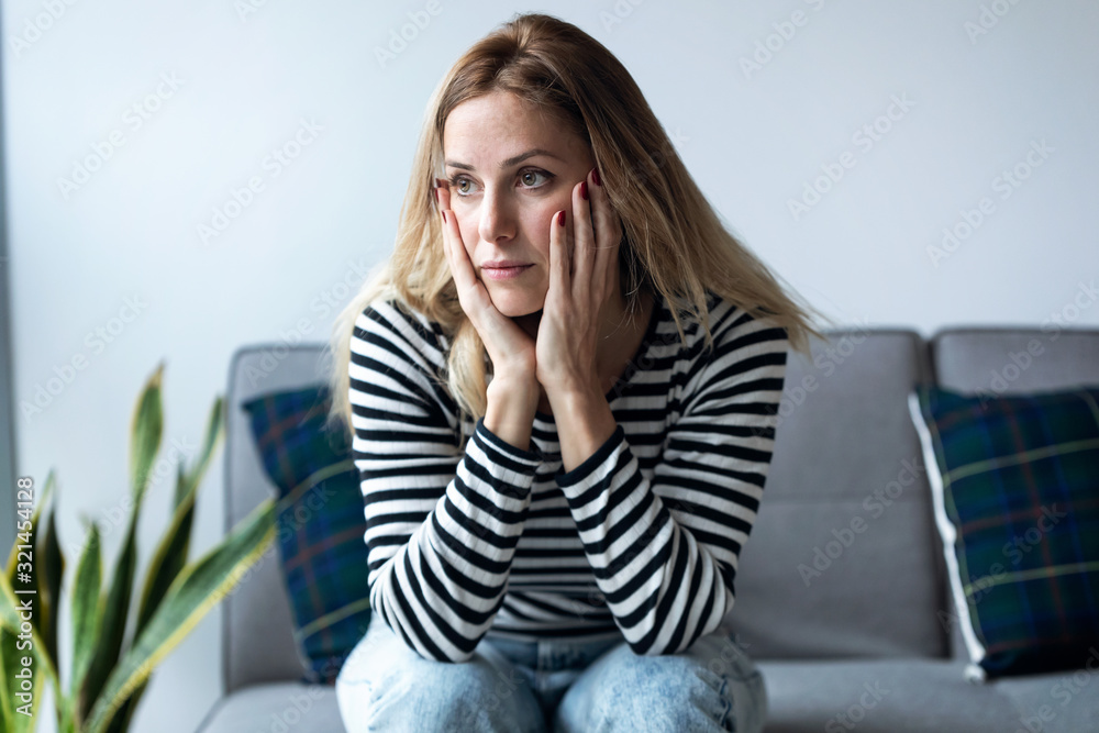 Depressed young woman thinking about her problems while sitting on the sofa at home. - obrazy, fototapety, plakaty 