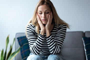 Depressed young woman thinking about her problems while sitting on the sofa at home.