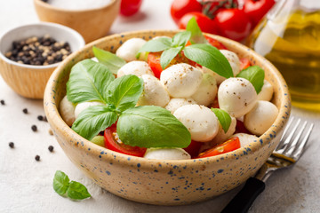 Wall Mural - Traditional Italian caprese salad with mozzarella cheese, cherry tomatoes and basil in ceramic bowl on concrete background. Selective focus.
