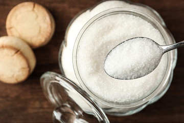 Taking spoon of sugar from glass bowl on wooden table, closeup