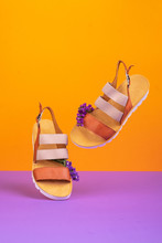 A Pair Of Dancing Yellow Female Leather Sandals With Purple Flowers On A Orange Lilac Background For A Banner With A Copy Space.