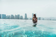  Woman swimming in roof top outdoor pool in Singapore.A young woman with a coconut in her hands is relaxing in the outdoor pool on the roof of the hotel with amazing views of the city's skyscrapers