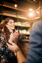 Poster - Beautiful caucasian smiling stylish woman  holding beer and chatting with friends. In background is bar counter. Pub interior.