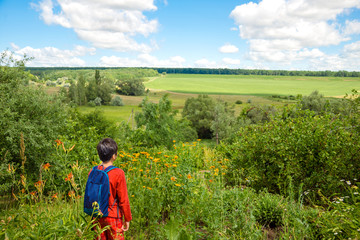 Young boy with backpacks  admiring nature - fields, forests and blue sky with light clouds