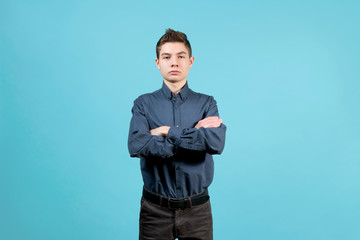Wall Mural - A teenager in a blue shirt with folded arms on his chest stands on a blue background with a serious face