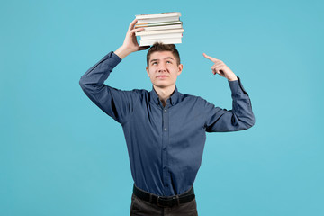 Wall Mural - A teenager in a blue shirt with discontent holds a stack of books on his head and points a finger at it.