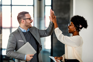 Wall Mural - Coworkers celebrating achievement at office. Celebrating success. Happy young man standing in office and giving high five to his colleagues. Two business people high-five. Job well done