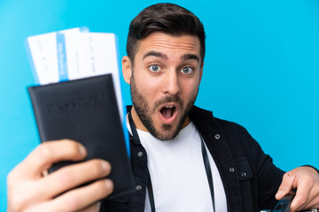 Traveler man holding a suitcase and a passport over isolated blue background