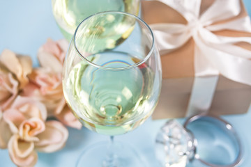 Two glasses with white grape wine with roses and gift box on the background. Romantic dinner concept.