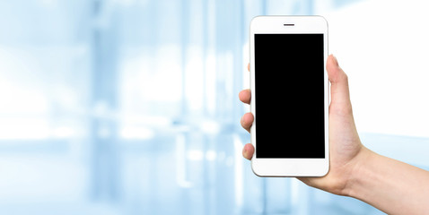 Wall Mural - woman hand holding a white smartphone with blank screen on a blurred background of a modern corporat
