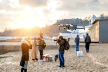 Shooting video and photo of drones closeup on sky background and people walking along the beach near the sea