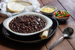 © Gener Vázquez - Plato de frijoles negros con salsa mexicana tortillas y queso cotija en mesa de madera