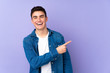© luismolinero - Teenager caucasian  handsome man isolated on purple background surprised and pointing side