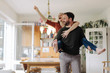 © Westend61 - Man carrying happy woman piggyback in their comfortable home