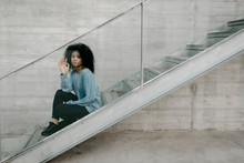 Beautiful Young Woman Sitting On Stairs Behind A Glass Pane