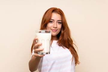 Wall Mural - teenager redhead girl holding a glass of milk over isolated background with happy expression