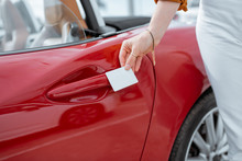 Woman opening car door with a plastic card, close-up on hands and door handle. Concept of keyless car access with a card