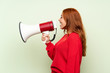 © luismolinero - Teenager redhead girl with sweater over isolated green background shouting through a megaphone