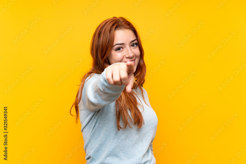 Teenager redhead girl over isolated yellow background points finger at you with a confident expression - obrazy, fototapety, plakaty 
