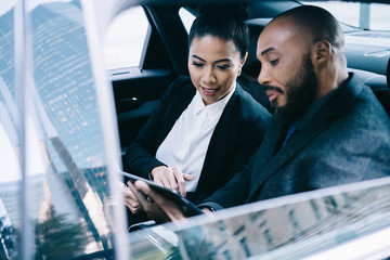 Pensive multiracial business partners interacting with digital tablet in car