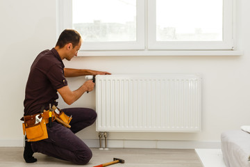 Man is repairing radiator battery in the room. Maintenance repair works renovation in the flat. Heating restoration. Wrench in hands