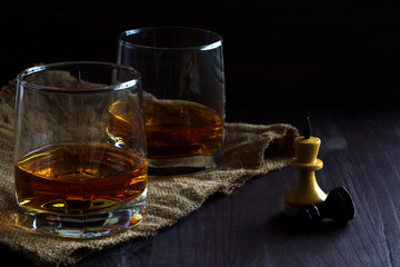 alcoholic drinks. glass of whiskey with ice with chess pieces on a black background. two glasses of whiskey on a wooden table with a burlap chess queen and a pawn. horizontal orientation