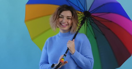 Wall Mural - Rainbow umbrella. Portrait of happy smiling young sexy girl rotating rainbow umbrella in blue sweater on blue background slow motion. Pleasure. Emotions of people. Monotone. Blue pantone