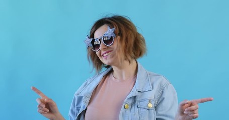 Wall Mural - Portrait of happy smiling young sexy girl in star sunglasses listening to music dancing and waving her hands rhythmically on blue background. Pleasure. Emotions of people