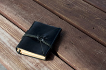 A Closed Leather Bound Black Journal Outdoors On Table, Wrapped With Cord  With Copy Space.