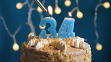 Birthday Cake With 34 Number Candle On Blue Backgraund Set On Fire By Lighter. Close-up