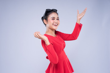 An attractive woman wearing casual red attire with gestures and poses towards copyspace isolated on grey. Good for technology, transportation, business or finance concept