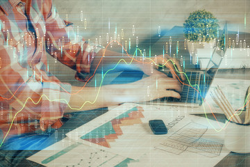 Double exposure of stock graph with businessman typing on computer in office on background. Concept of hard work.